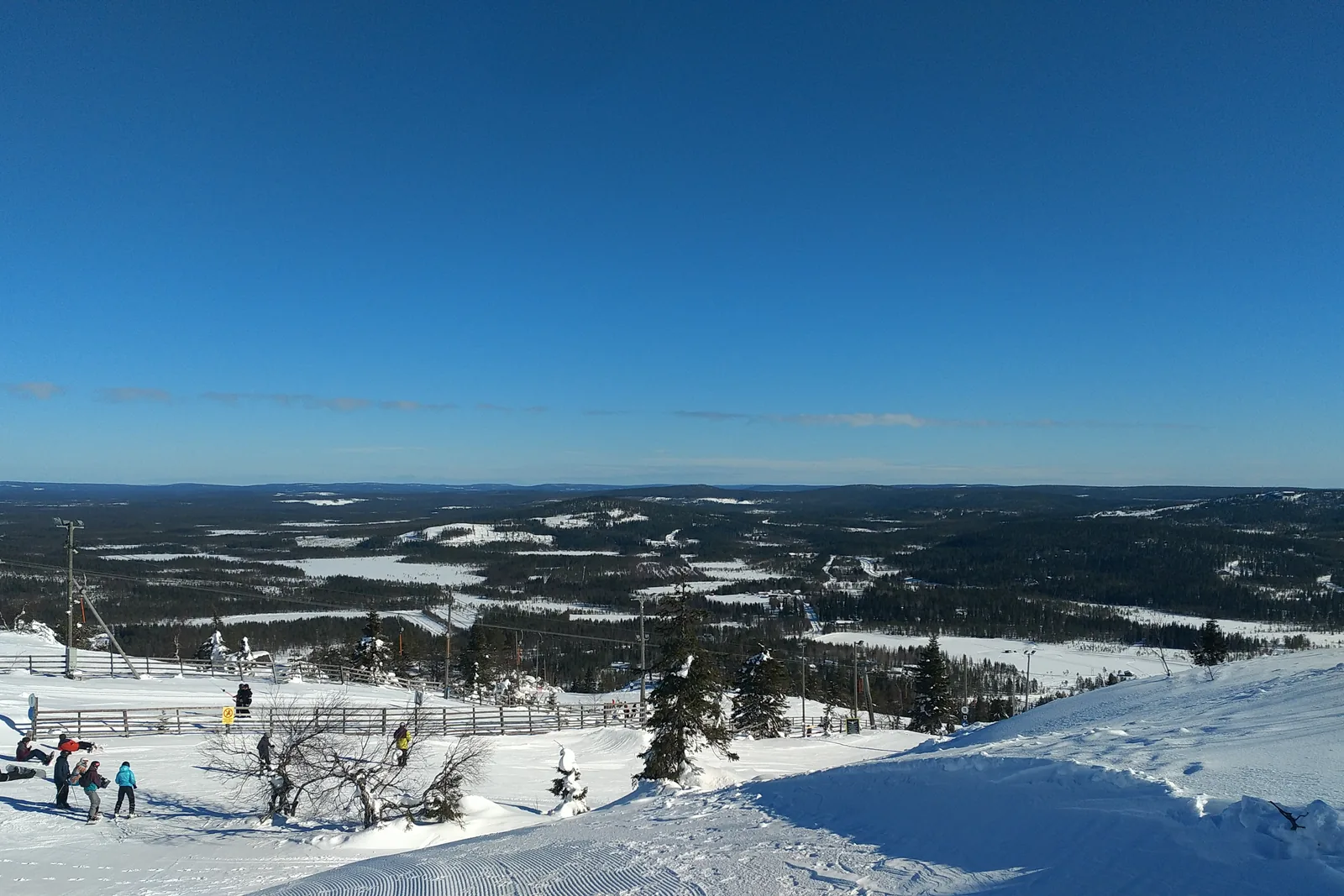 Laskettelijoita loivalla rinteellä, alapuolella avautuu metsien ja järvien maisema